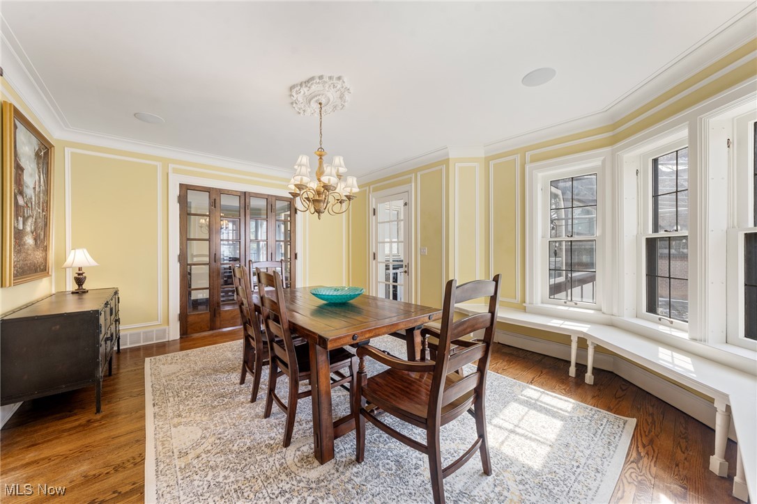 Dining room with a wooden table, ornate chandelier, yellow paneled walls, and tall windows.