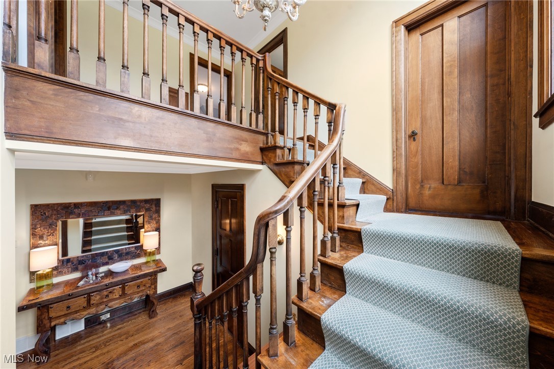 Grand wooden staircase with patterned carpet, an upper landing, and a console table beneath it.