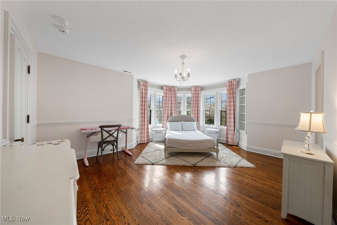 Bedroom with a white bed, bay windows framed by pink plaid curtains, and polished hardwood floors.