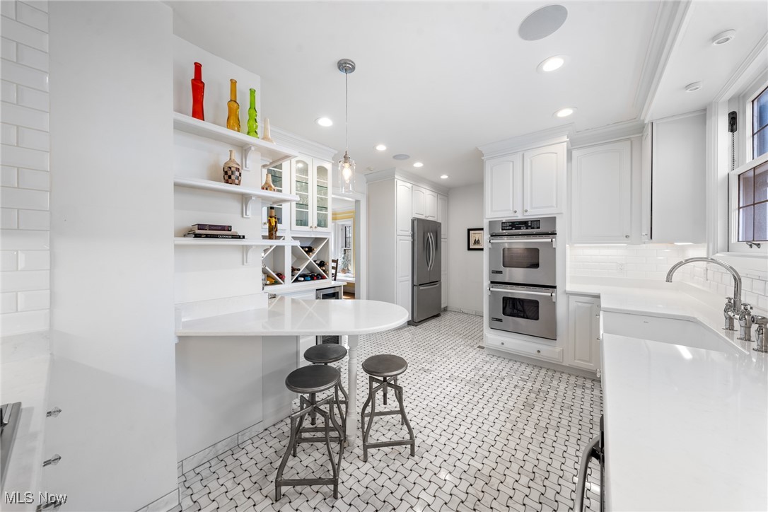 Bright white kitchen with stainless steel double ovens, patterned tile flooring, and a peninsula with three stools.