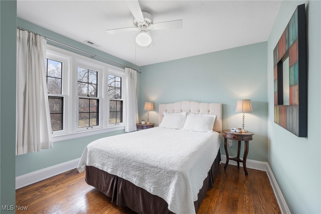 Bedroom with a white bed, pale aqua walls, hardwood floors, and three windows.