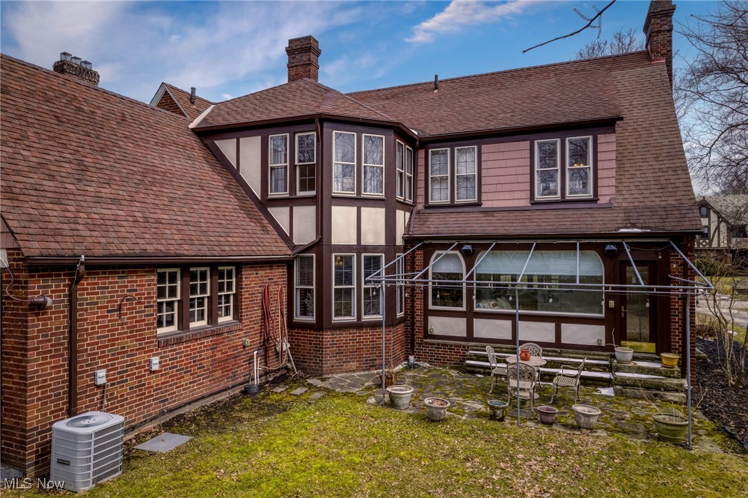 Rear of a brick home with a stone courtyard, covered patio, and outdoor seating.