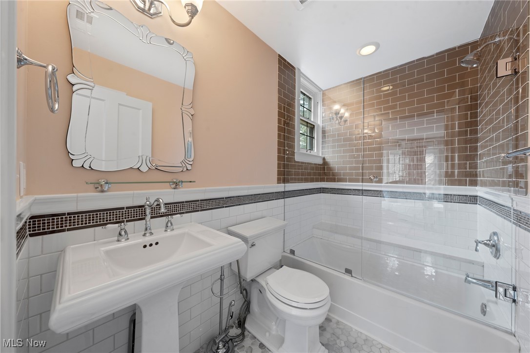 Bathroom with a pedestal sink and glass-enclosed tub lined with glossy brown tile.