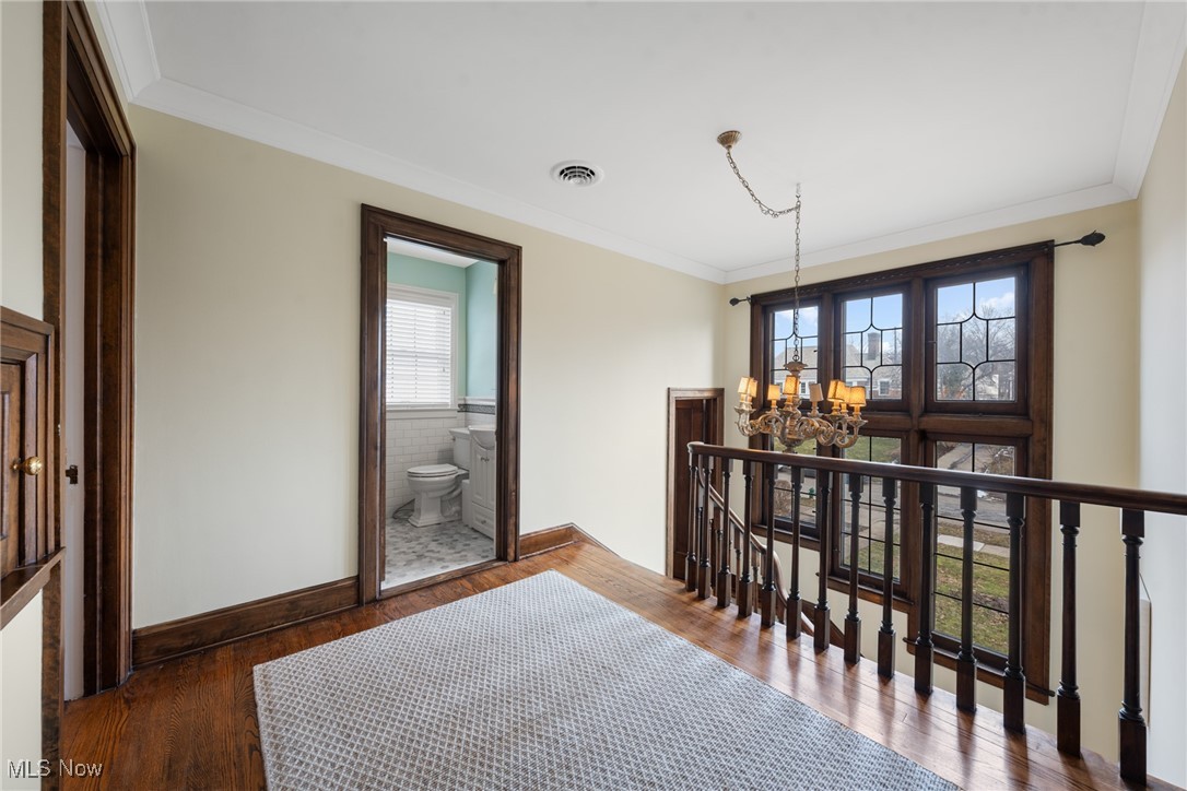 Upstairs landing with dark wood floors, a chandelier, and large windows beside an open bathroom doorway.