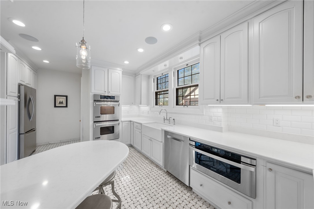 White kitchen with a large peninsula, stainless steel appliances, and patterned tile floor.