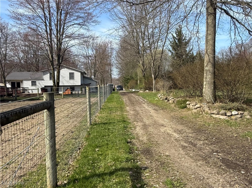Gravel driveway beside a wire fence leading toward a white two-story house and leafless trees.