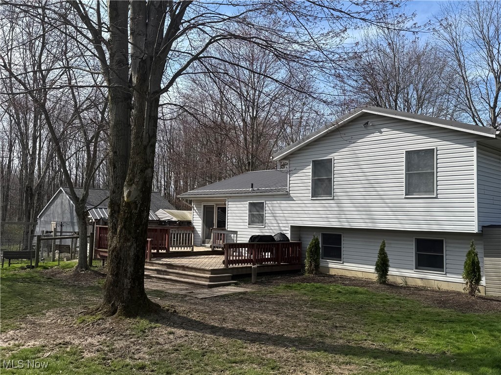 Gray-sided home with a wooden deck, leafless trees, and a small outbuilding in the yard.