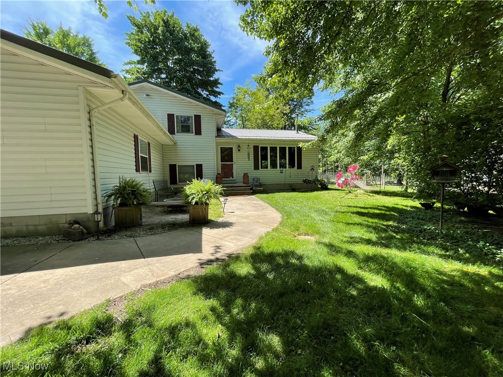 House rear exterior with a curved walkway, broad lawn, and mature shade trees.