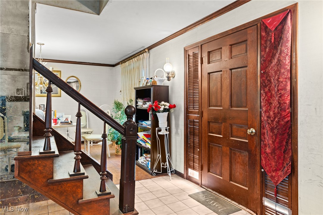 Entry hall with a dark wood staircase, paneled front door, tiled floor, and red patterned curtain.