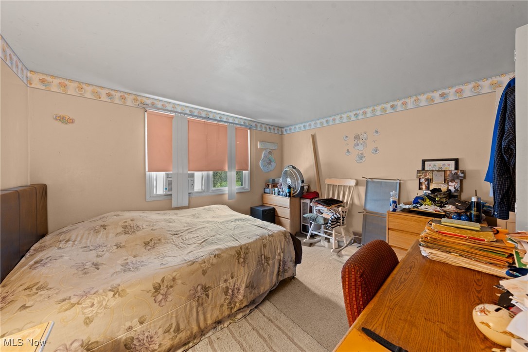 Bedroom with a floral bed, peach window shades, rocking chair and cluttered desk.