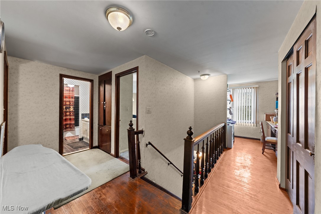 Upper-floor hallway with dark wood stair railing, partly visible bed, and bathroom doorway.