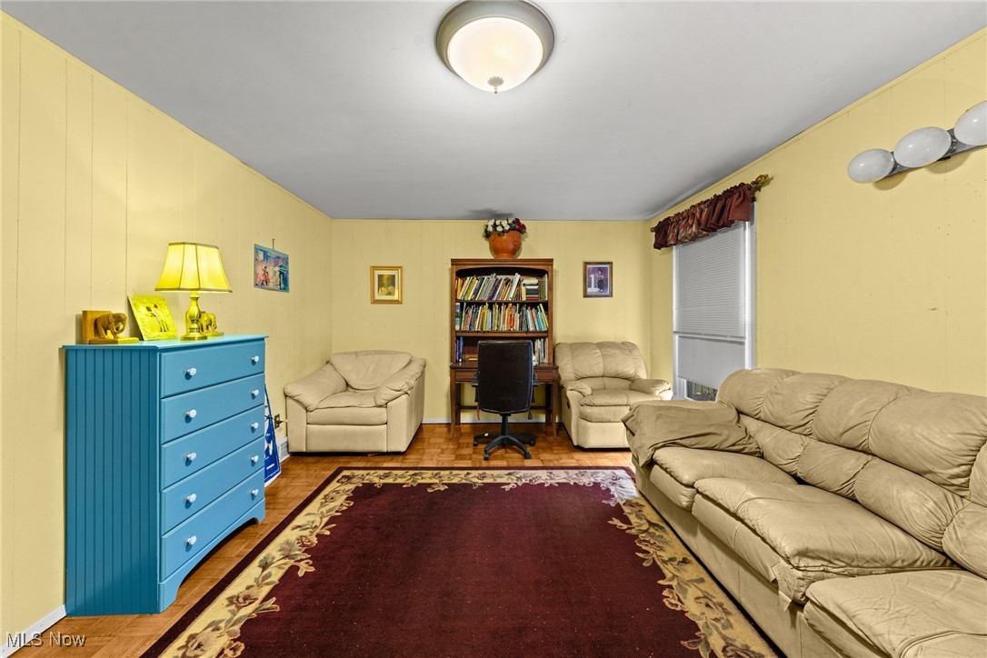 Furnished living room with beige leather sofas, a bookcase and desk, and a burgundy rug.