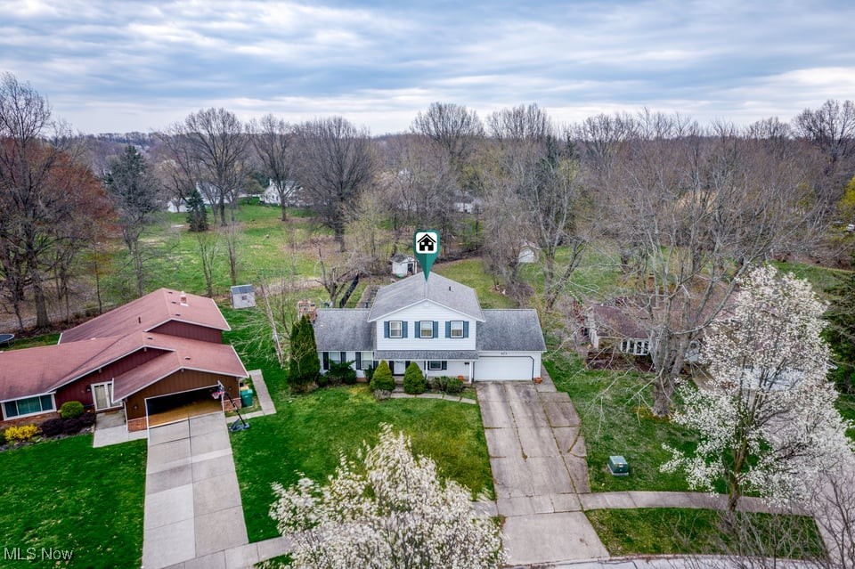 Aerial view of a two-story gray-and-white home with an attached garage and spring trees.
