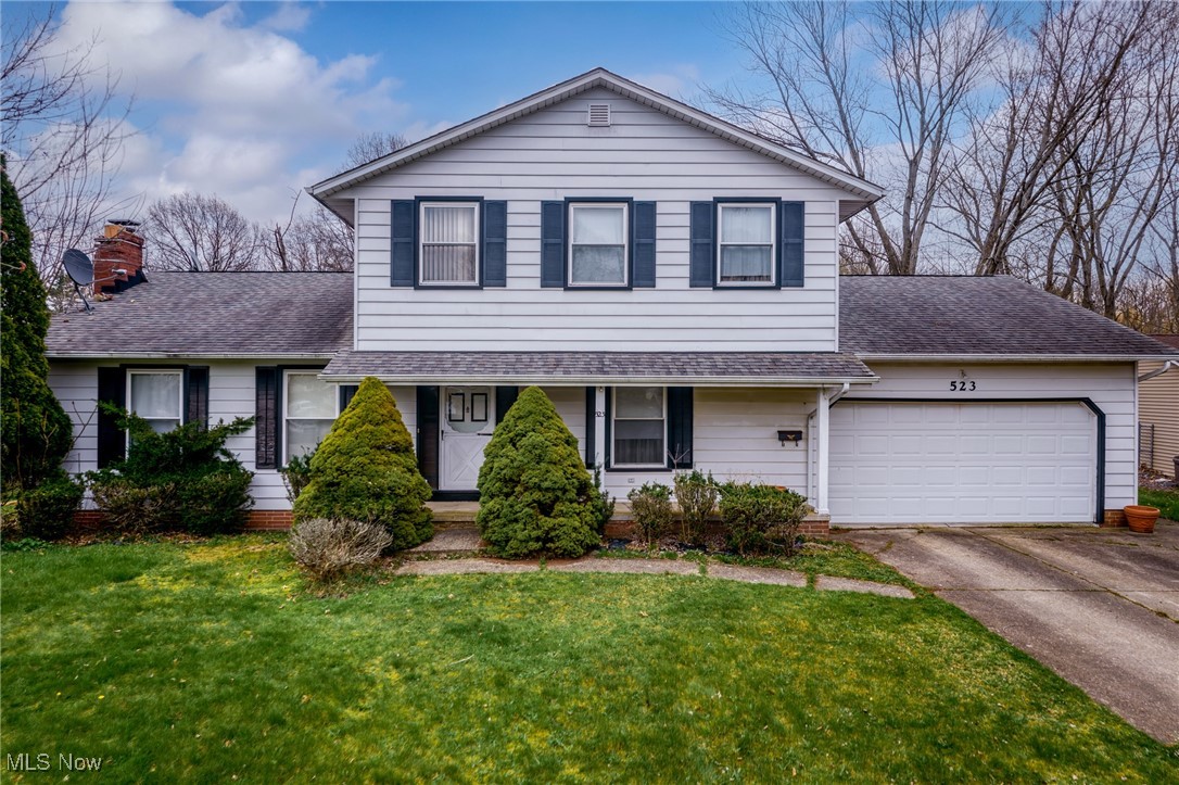 Two-story white house with dark shutters, attached garage, and shrubs along the front lawn.