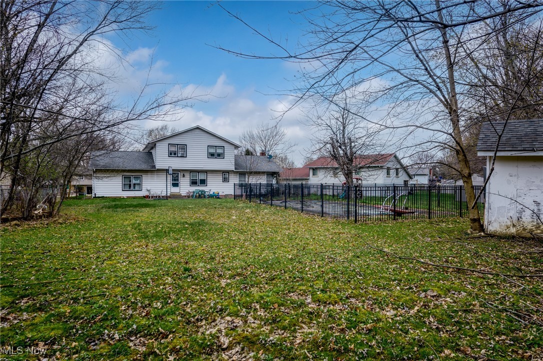 Back of a white-sided two-story home with a fenced yard and leaf-covered lawn.