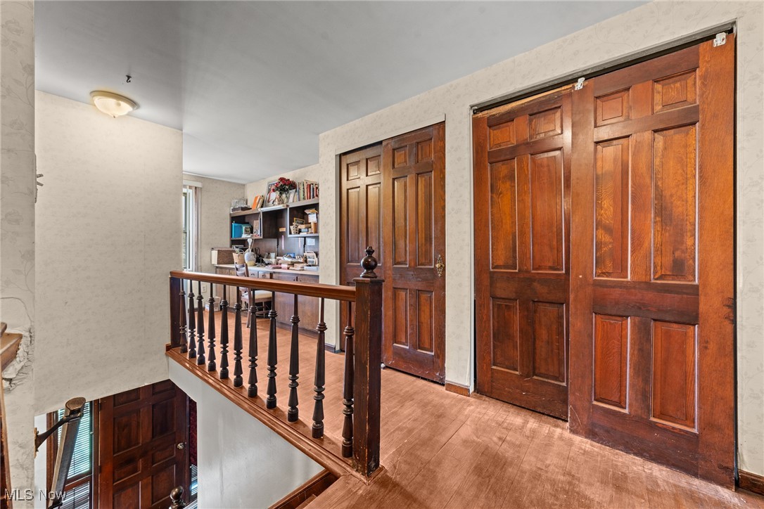 Upstairs landing with dark wood paneled doors, wood flooring, and a stair railing.
