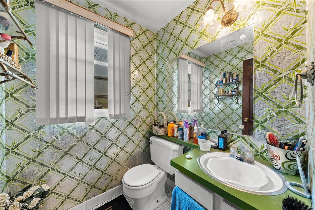 Bathroom with green geometric wallpaper, green vanity, white sink, and toilet.