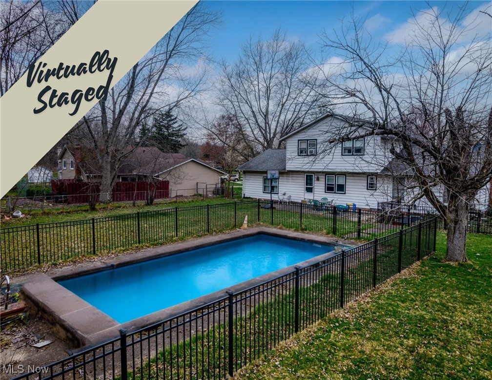 Backyard swimming pool enclosed by a black metal fence, with a white two-story house behind it.