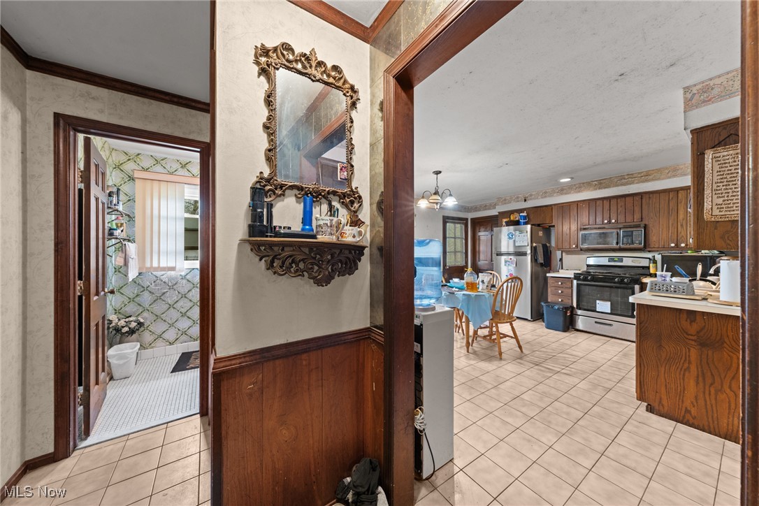 Kitchen with dark wood cabinets and appliances, viewed beside a tiled hallway and small bathroom.