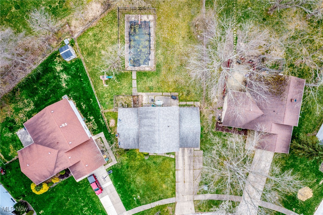 Aerial view of a house with a rectangular swimming pool, lawn, and neighboring homes.