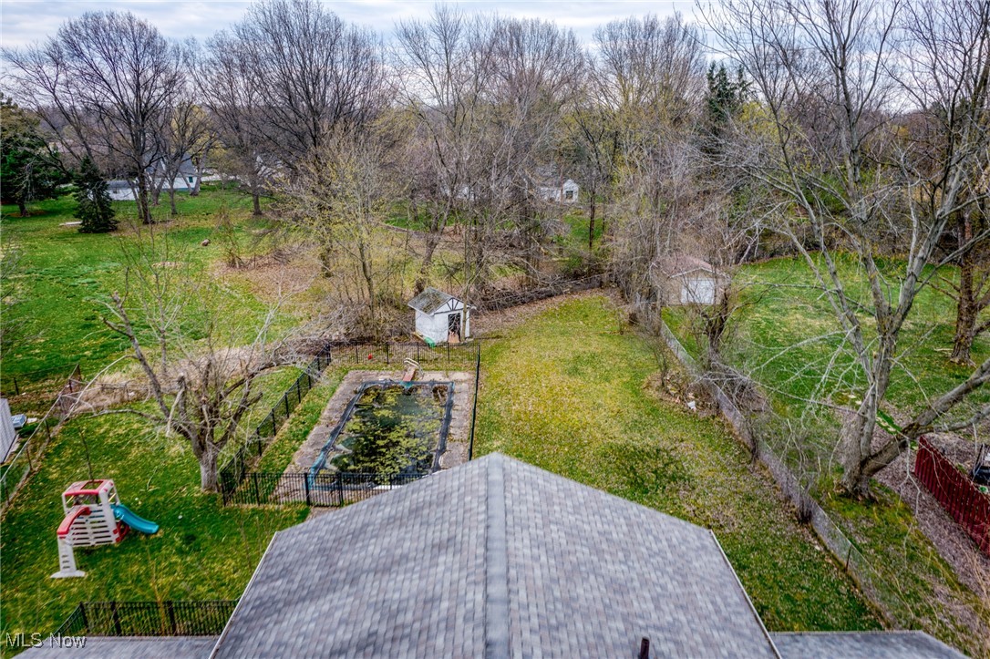 Aerial view of a backyard with a fenced pool, shed, playset, and leafless trees.
