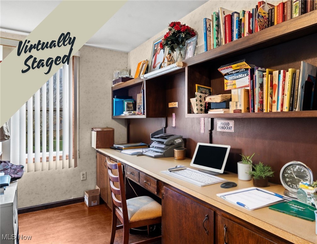 Home office with a long built-in desk, dark wood shelves, and vertical blinds.