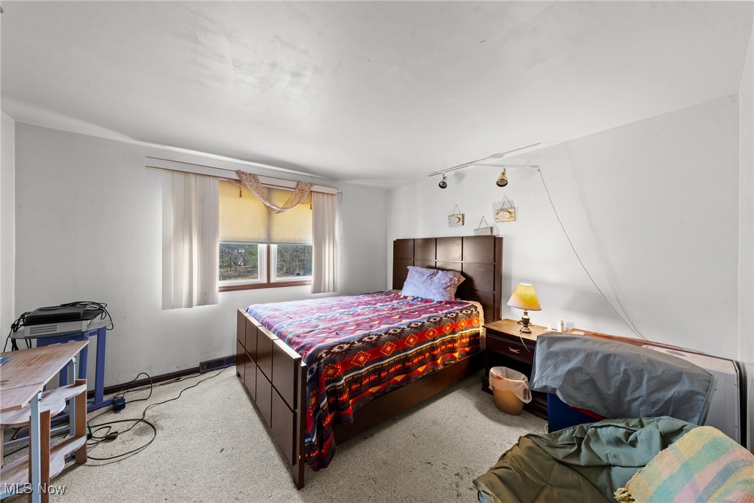 Bedroom with a dark wood bed, colorful patterned bedding, and a window with vertical blinds.
