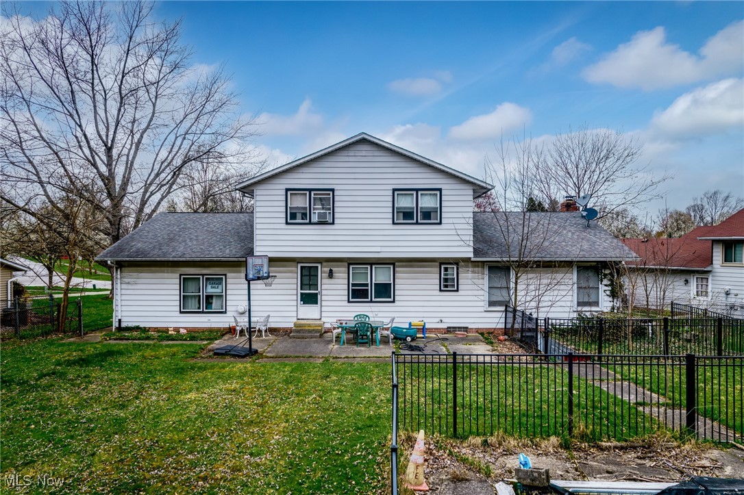 Rear of a white two-story house with a patio, basketball hoop, and fenced backyard.
