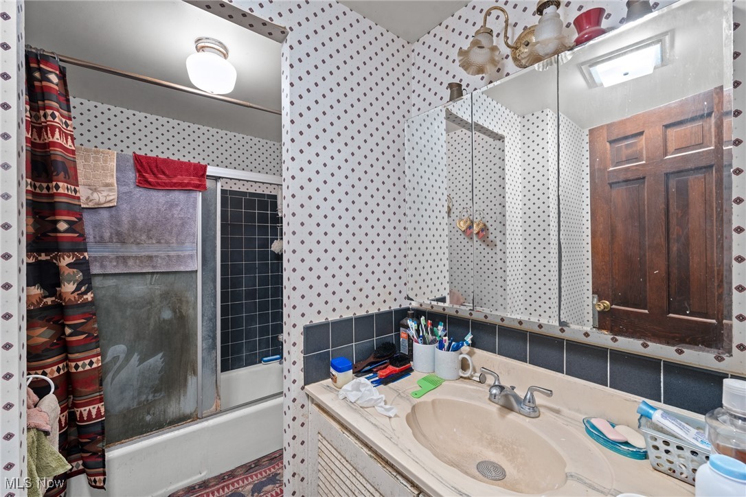 Bathroom with a tub and shower, patterned curtain, and single-sink vanity.