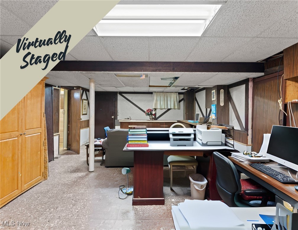 Basement office with desks and computers, wood-paneled walls, and exposed support beams.