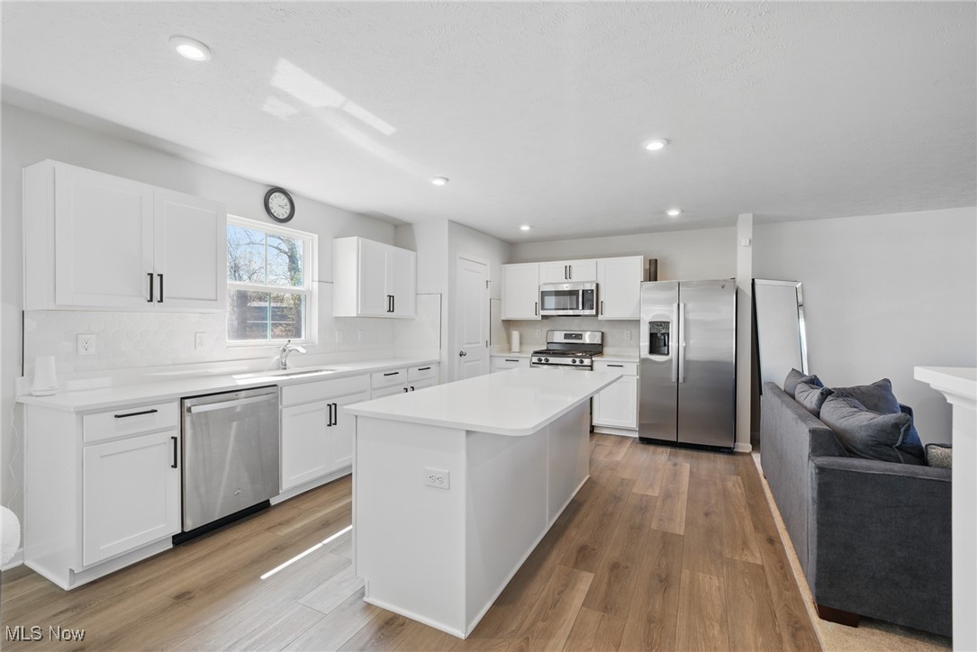 Open kitchen with a large white island, stainless steel appliances, and a gray sofa.