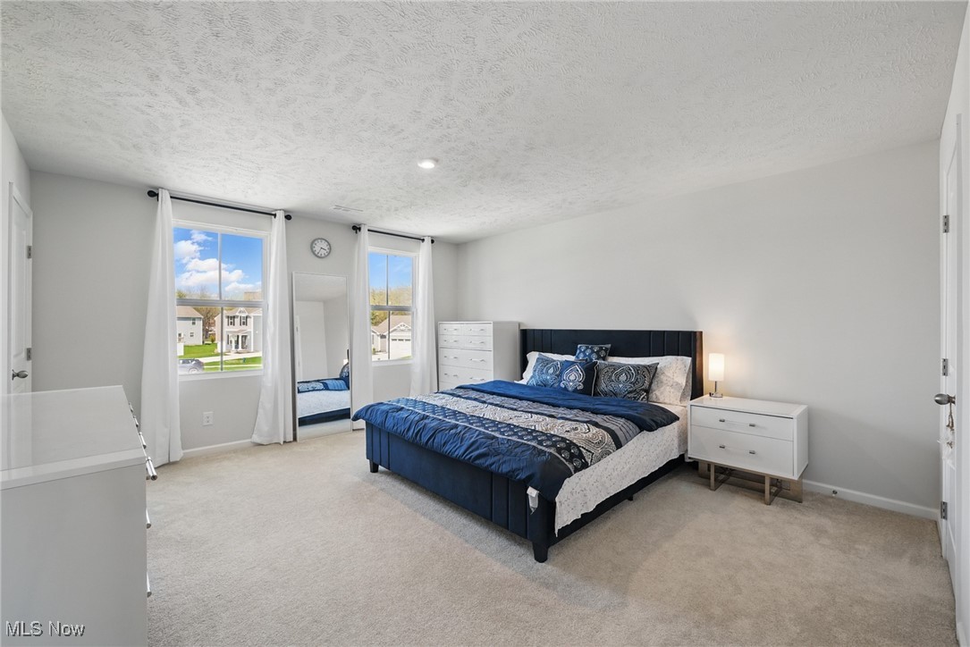 Bedroom with a blue upholstered bed, patterned bedding, and two curtained windows.