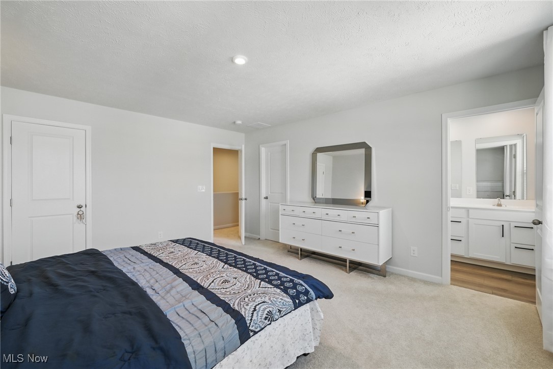 Furnished bedroom with a patterned bedspread, white dresser, and doorway to an adjoining bathroom.