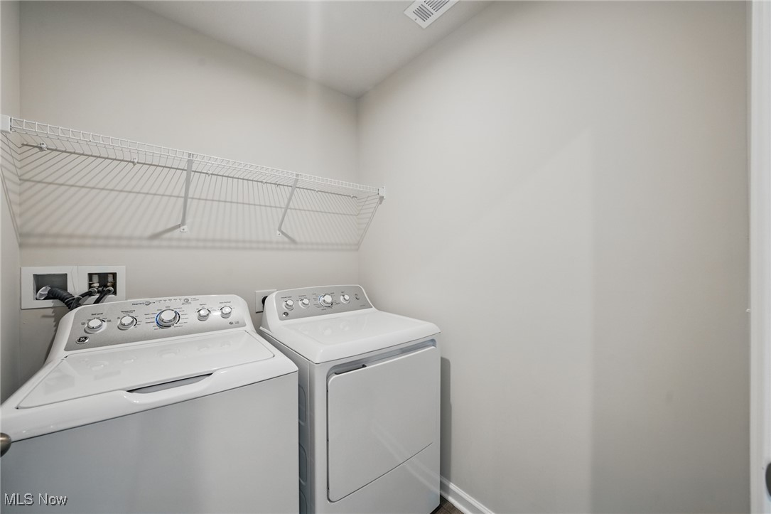 Laundry room with a top-loading washer, matching dryer, and long wire shelf.