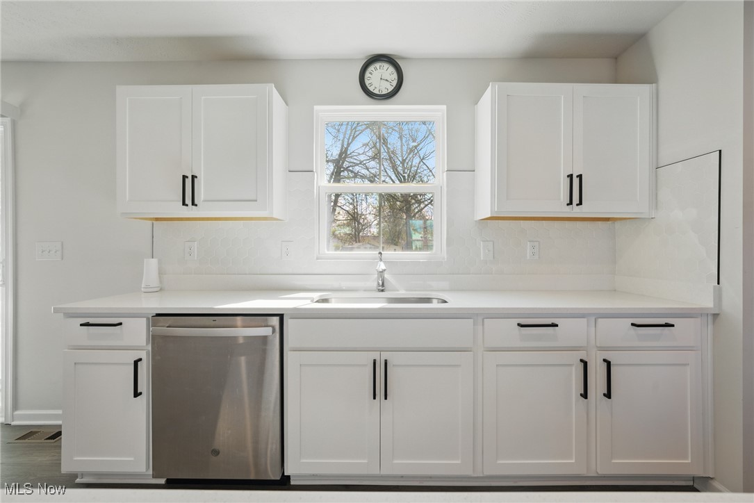 Bright white kitchen with shaker cabinets, a hexagonal tile backsplash, and a window above the sink.