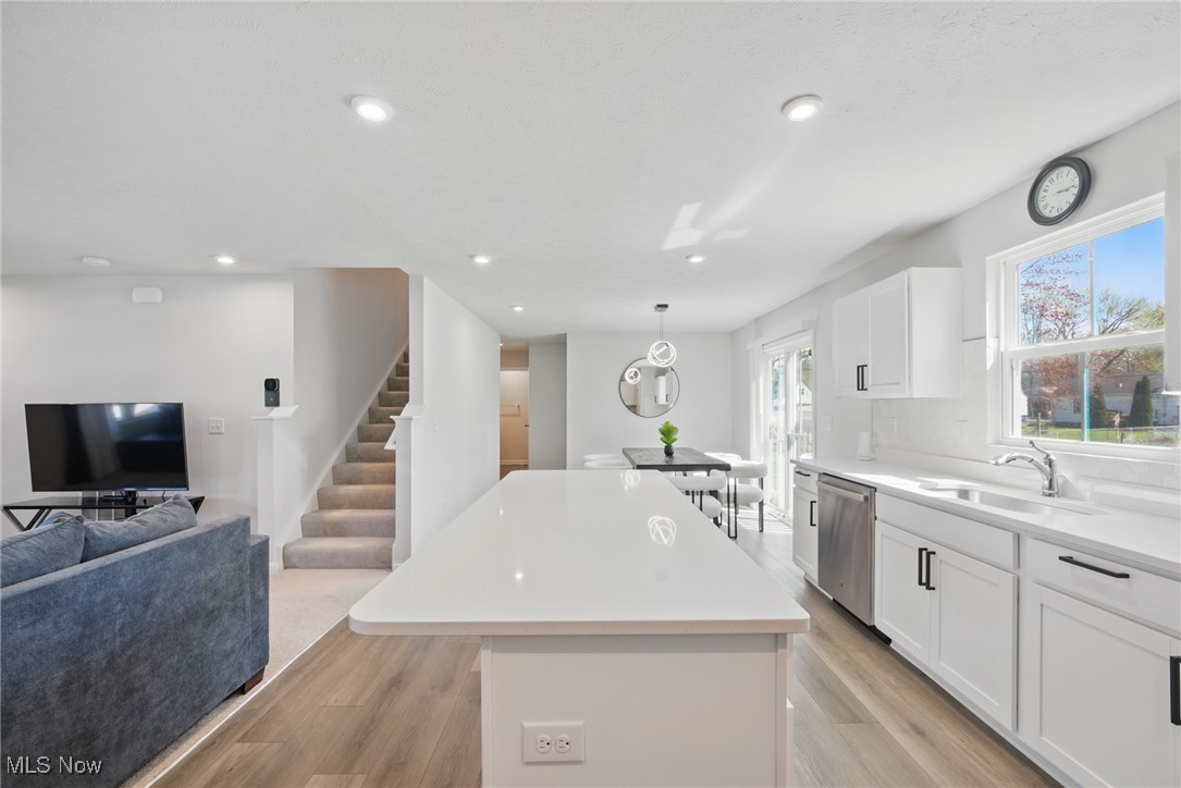 Open-plan kitchen with a large white island, stainless steel dishwasher, and adjoining living area.