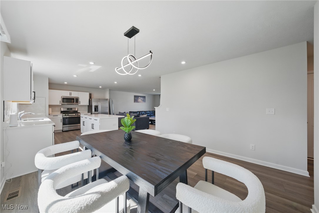 Dining area with a dark wood table, white chairs, and an open kitchen with stainless steel appliances.
