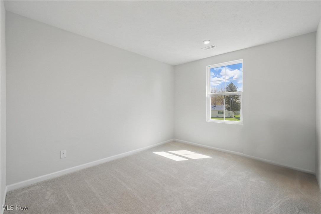 Empty carpeted bedroom with gray walls and sunlight falling through a single window.