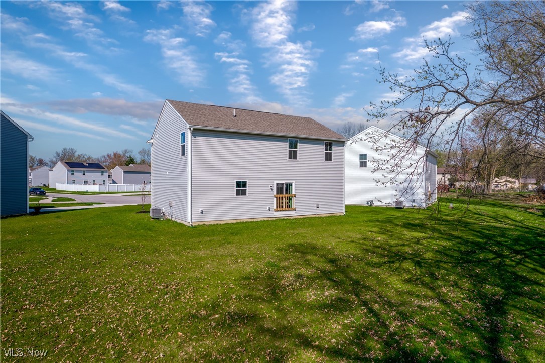 Rear of a two-story gray-sided house with a small deck and broad green lawn.