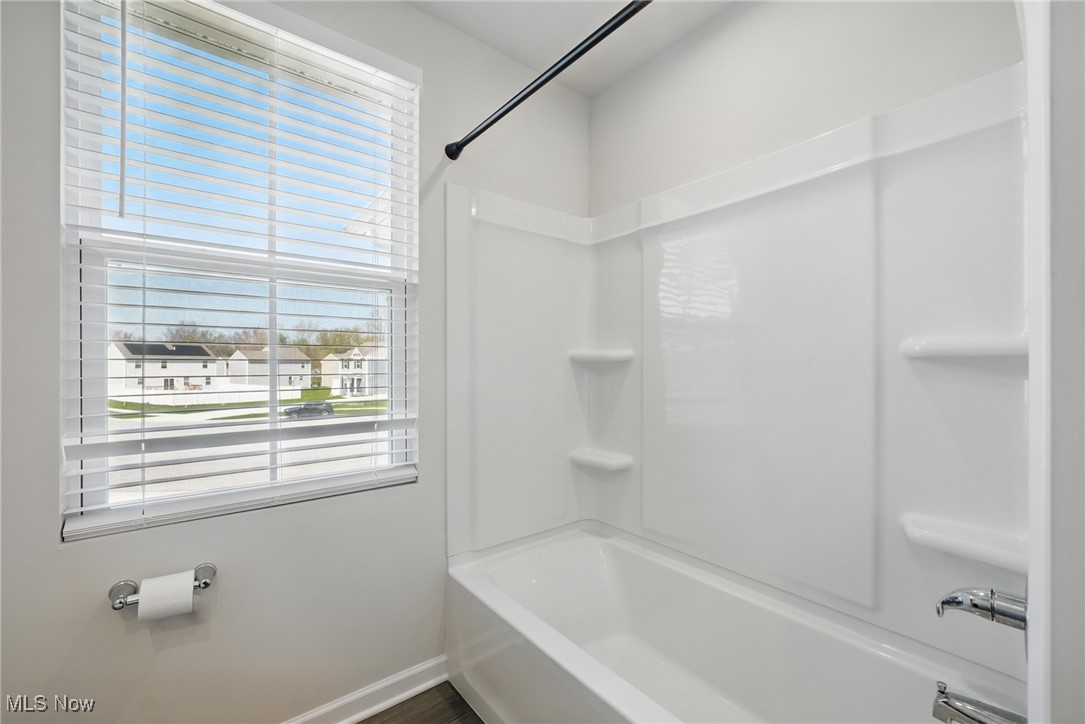 Bathroom with a white tub and shower surround beside a window with blinds.