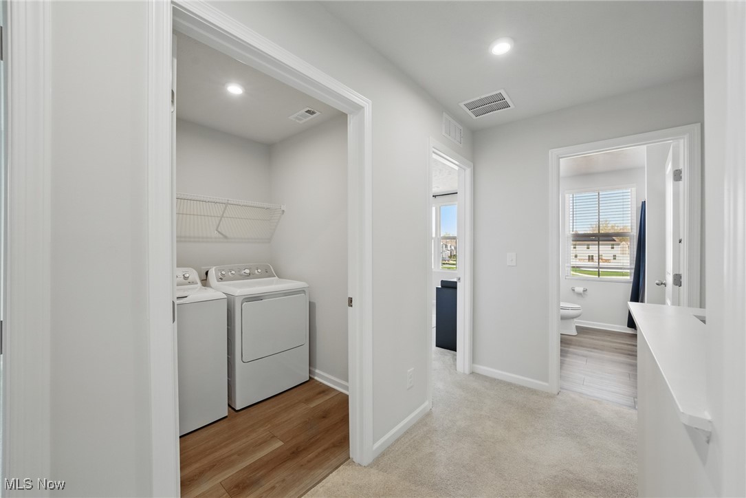 Laundry area with white washer and dryer, opening onto a carpeted hall and bathroom.