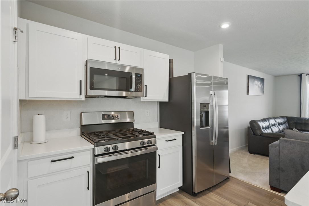 Renovated kitchen with white cabinets, stainless steel appliances, and an adjoining living area.