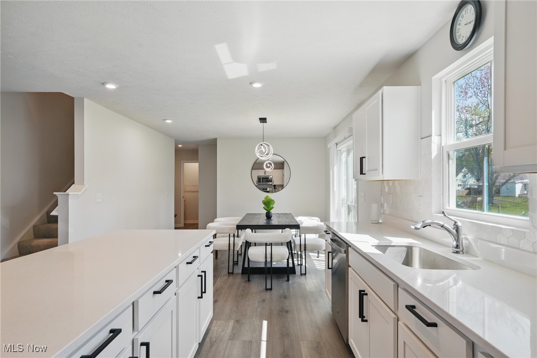 Bright white kitchen with a large island opening to a dining area with wide windows.