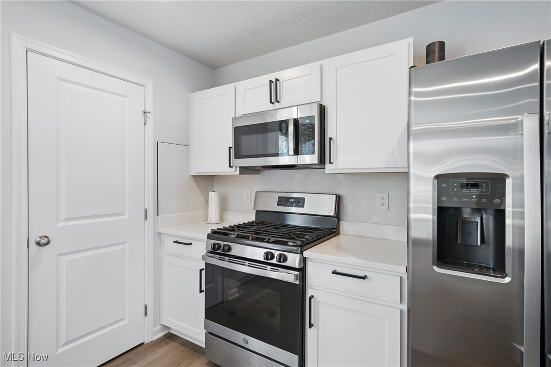 Kitchen with white shaker cabinets, stainless steel appliances, gas range, and hexagonal tile backsplash.