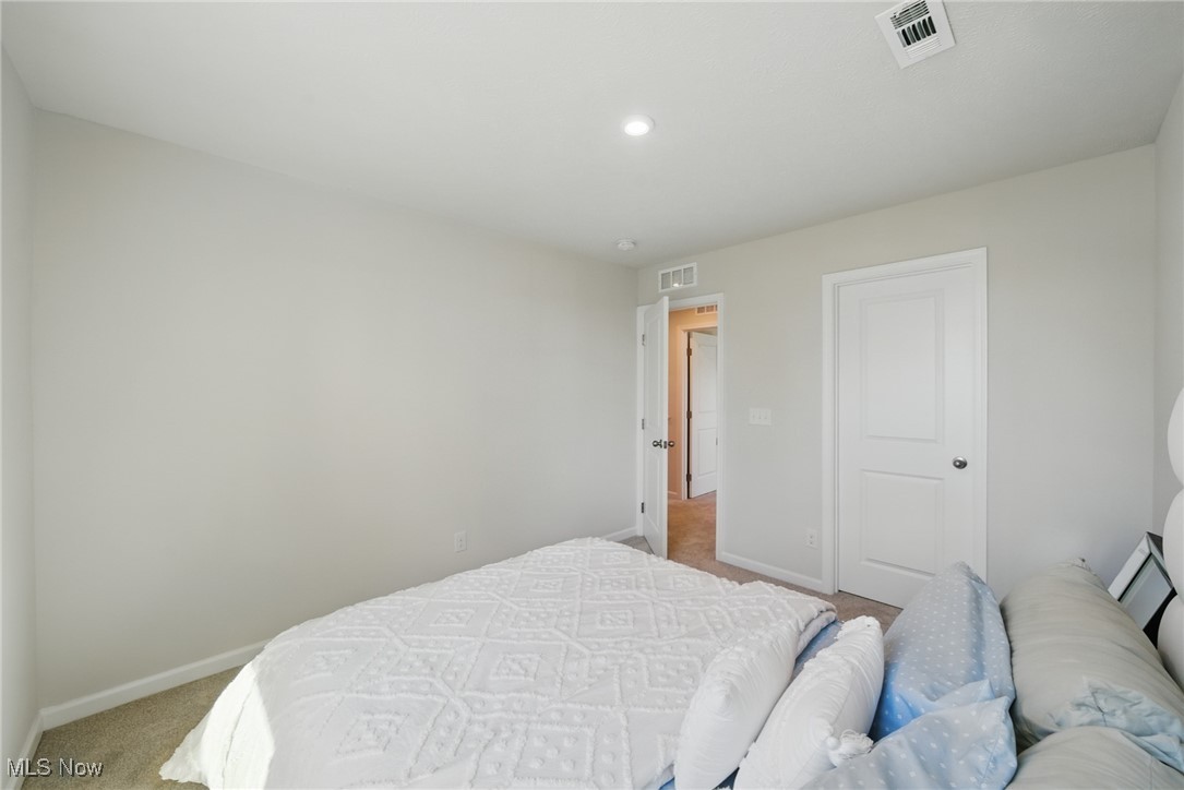 Bedroom with a white quilted bed, neutral walls, and an open doorway to the hall.