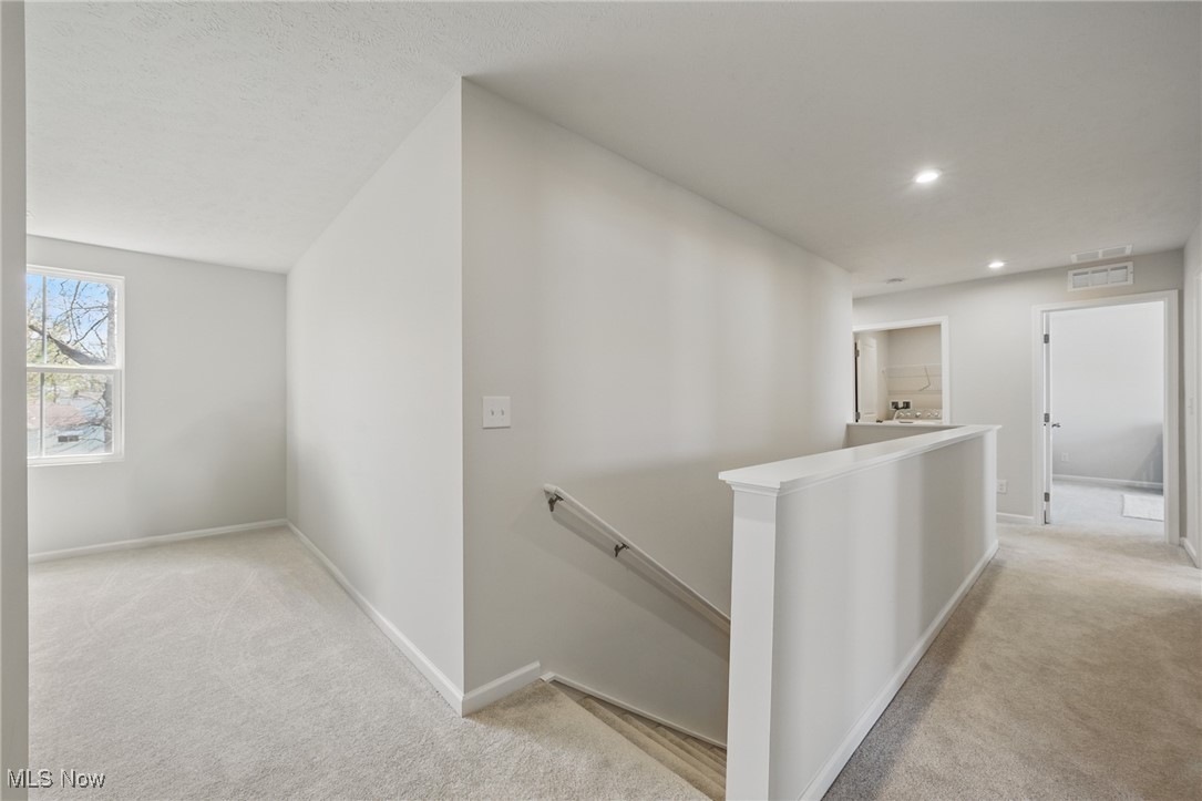 Carpeted upstairs landing overlooking a stairwell, with a window and doorways to adjoining rooms.