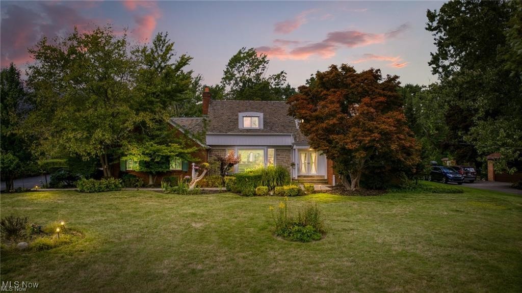 House with lit windows, mature trees, and a broad lawn beneath a pink dusk sky.