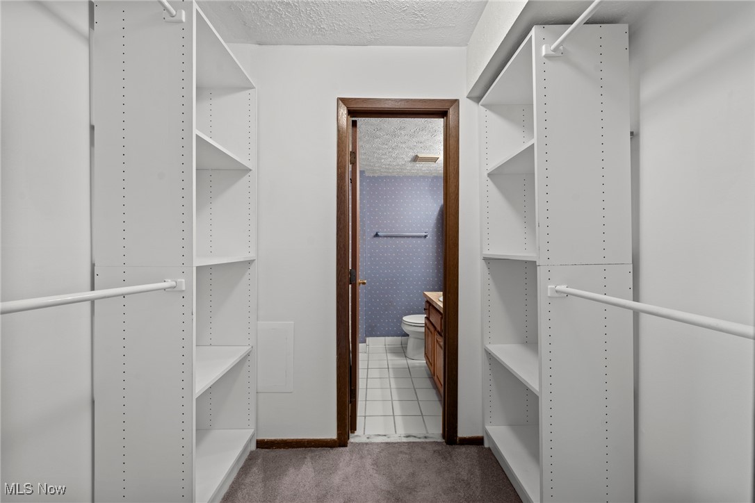 Walk-in closet with white adjustable shelving and hanging rods, opening into a bathroom.