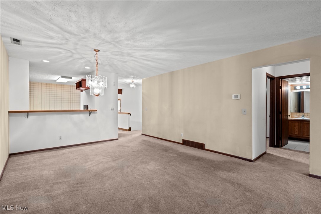Vacant living area with beige carpet, a kitchen pass-through, and an open doorway to a bathroom.