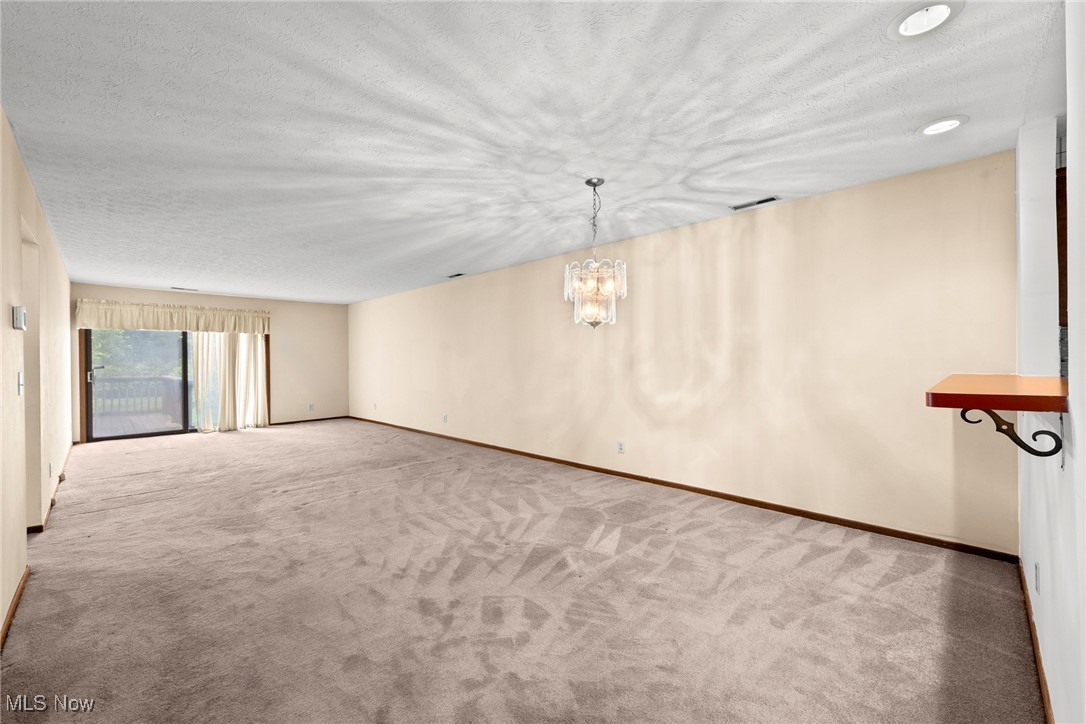 Unfurnished living room with patterned carpet, a chandelier, and a sliding glass door to a deck.